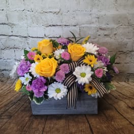 Mixed bouquet of yellow roses, daisies, and purple flowers in a wooden box