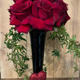 Red roses in a tall black vase with trailing greenery and a glittery heart
