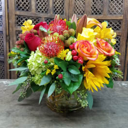 Mixed bouquet in a glass vase with roses, sunflowers, and orchids