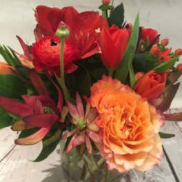 Compact red and orange flower arrangement in a clear glass cylinder vase