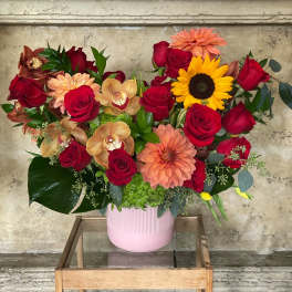 Mixed bouquet with red roses, peach dahlias, and a sunflower in a pink vase