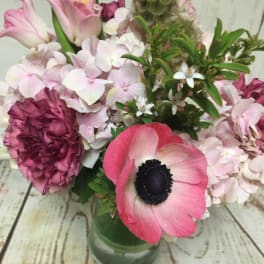 Compact pink and white mixed flower arrangement in a clear glass vase on a rustic wood surface
