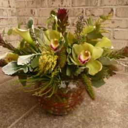 Low arrangement of green cymbidium orchids and pale calla lilies in a clear glass bowl vase
