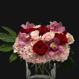Bouquet of red and pink roses with orchids in a clear glass vase