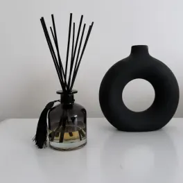 Black reed diffuser bottle with a round black vase beside it