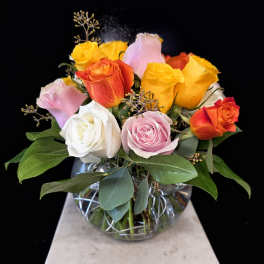 Mixed roses in a clear glass vase with green foliage