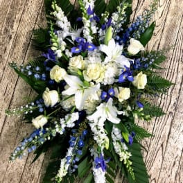White lilies and blue flowers arranged in a cross shape