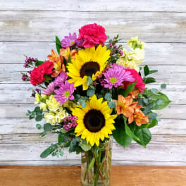Mixed bouquet with sunflowers, pink and orange blooms in a glass vase
