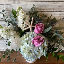 Pink roses and white flowers arranged with a starfish in a white vase