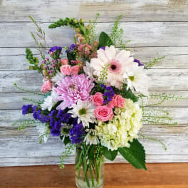 Mixed bouquet of pink, white, and purple flowers in a clear glass vase
