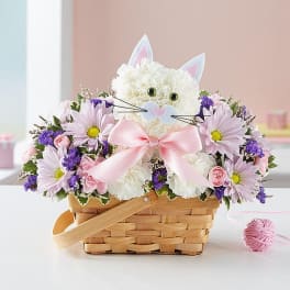 White cat-shaped flower arrangement in a wicker basket with pink and purple flowers