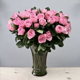 Large arrangement of pink roses in a tall clear glass vase against a gray background