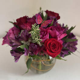 Bouquet of red roses and purple flowers in a glass vase with a butterfly decoration