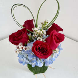 Red roses with blue hydrangea and white filler in a heart-shaped design