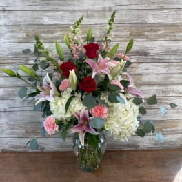 Bouquet of red roses, pink lilies, and white hydrangeas in a glass vase