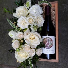 White rose arrangement in a wooden box with a wine bottle