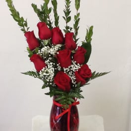 Red roses arranged in a red glass vase with baby's breath