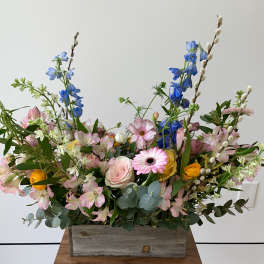 Mixed bouquet in a rustic wooden box with pink, blue, and yellow flowers