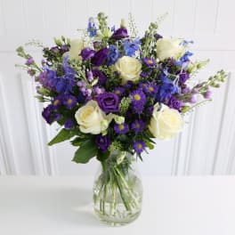 Bouquet of white roses and purple-blue flowers in a clear glass vase