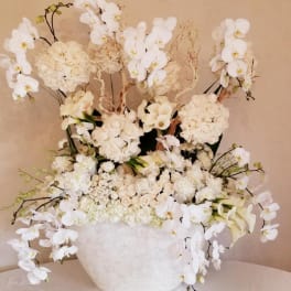 Large white floral arrangement in a white vase with orchids and roses