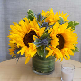 Sunflower arrangement in a green glass vase with a small candle beside it