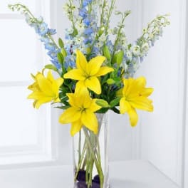 Yellow lilies and blue delphinium in a clear glass vase