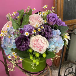 Bouquet of pink and purple roses with blue hydrangeas in a green container
