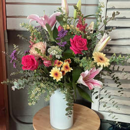 Mixed bouquet of pink lilies, roses, and daisies in a white vase