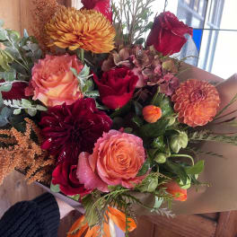 Bouquet of orange, red, and pink flowers wrapped in brown paper
