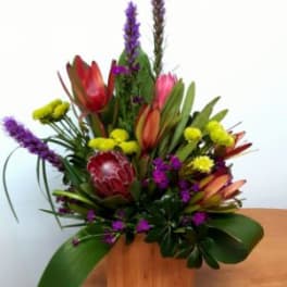 Tropical floral arrangement with purple spikes and red-orange blooms in a wooden box