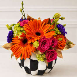 Bright orange gerbera and pink roses in a black-and-white checkered pumpkin container