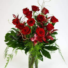 Red roses arranged in a clear glass vase with tropical foliage