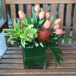 Pink tulips and tropical flowers arranged in a square glass vase