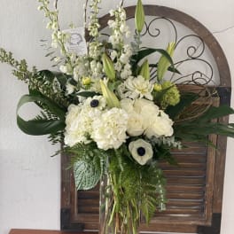 White floral arrangement in a clear glass vase with tall stems and greenery