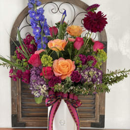 Colorful mixed flower arrangement in a white vase with a ribbon bow