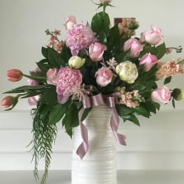 Pink roses and mixed blooms arranged in a white vase with a ribbon