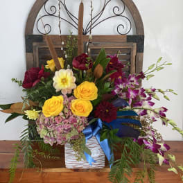 Mixed floral arrangement with yellow roses and purple orchids in a white vase