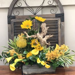 Yellow flowers arranged with calla lilies in a rustic wooden container