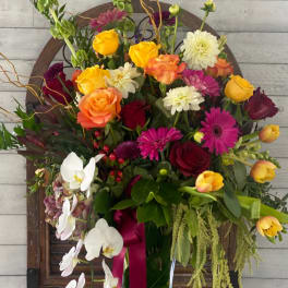Mixed bouquet in a tall glass vase with roses, orchids, and bright daisies