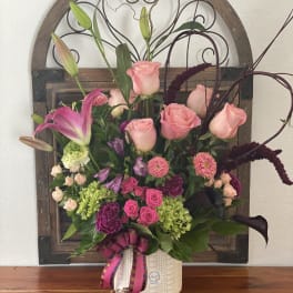 Pink roses and lilies arranged in a white vase with ribbon