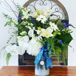 White orchids and lilies arranged in a metal vase with blue ribbon