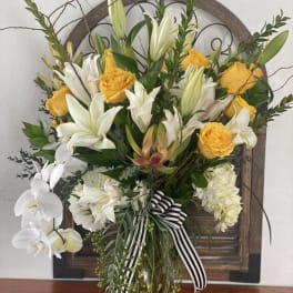 Yellow roses and white lilies in a glass vase with a striped ribbon