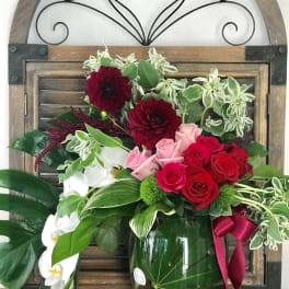 Bouquet of red and pink roses with white orchids in a glass vase