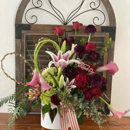 Mixed bouquet of red roses, pink lilies, and purple blooms in a white container