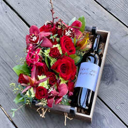 Red rose and orchid arrangement in a wooden box with a wine bottle