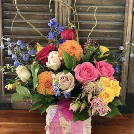 Mixed bouquet of roses, dahlias, and blue flowers in a white box with pink ribbon