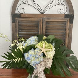 Hydrangea arrangement in a glass vase with a starfish accent and ribbon