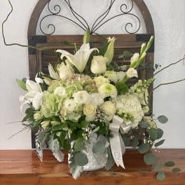 White floral arrangement in a white vase with lilies and roses