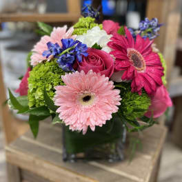 Mixed bouquet with pink gerbera daisies, roses, and blue flowers in a glass vase