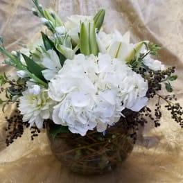 White floral arrangement in a round glass vase with lilies and hydrangeas